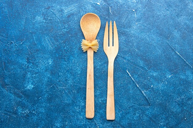 Top view wooden fork spoon farfalle on spoon on blue table free space