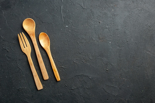 Top view wooden fork and spoons on dark table with free place