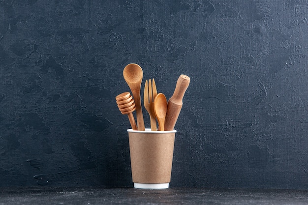 Top view of wooden kitchen spoons in a plastic coffee pot on dark wall