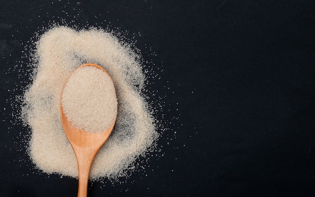 Top view of a wooden spoon with brown sugar on black background with copy space