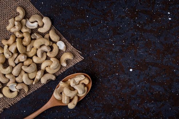 Top view of a wooden spoon with cashew on black background with copy space