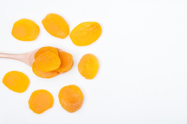 Top view of a wooden spoon with dried apricots on white background with copy space