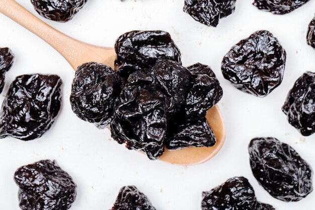 Top view of a wooden spoon with dried plums prunes on white background