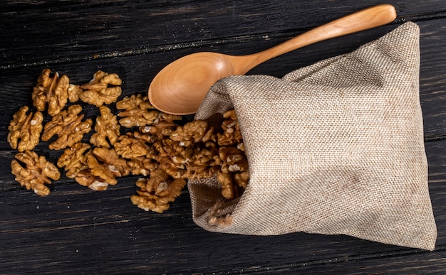 Top view of a wooden spoon with walnuts scattered from a sack on rustic