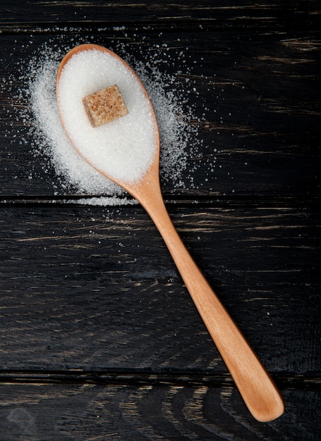Top view of a wooden spoon with white sugar and brown sugar cube on black background with copy space