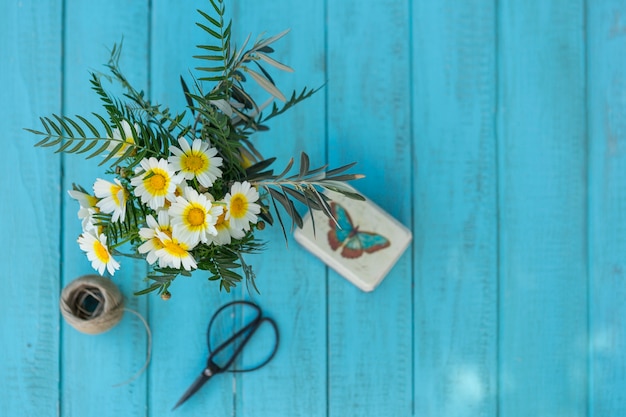 Top view of wooden surface with daisies, scissors and box