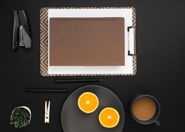 Top view of workspace with notepad and plate of orange slices