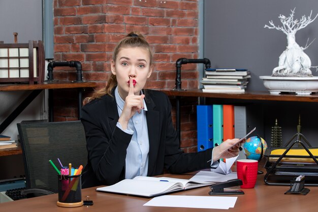 Free photo top view of worried woman sitting at a table and holding a document making silence gesture in the office