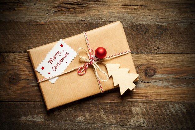 Top view of a wrapped Christmas present with a card that reads Merry Christmas, on a wooden surface