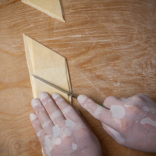 Top view xengel with dough with a rhombus and human hands and knife