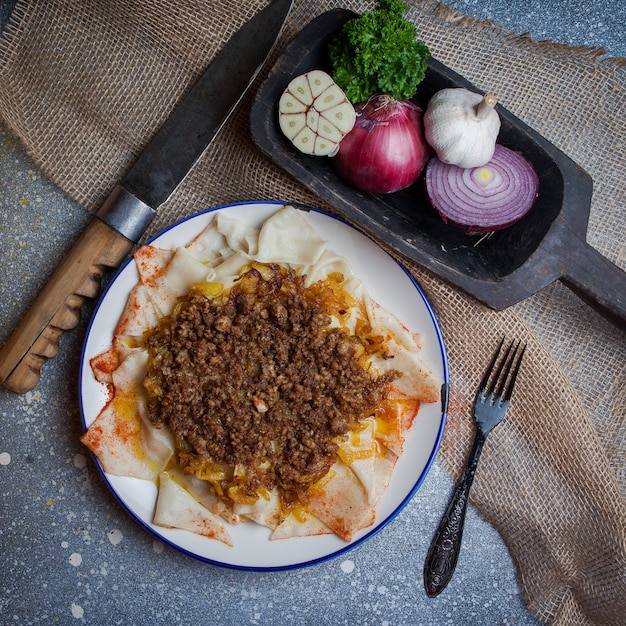 Top view xengel with yogurt and onion and garlic and fork and knife in round plate