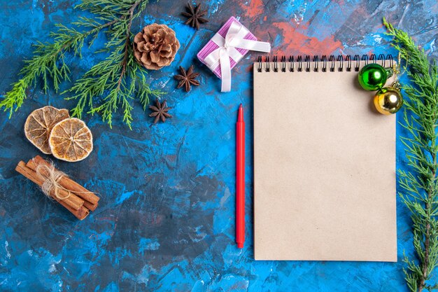 Top view xmas balls on a notebook pine tree branches cinnamon sticks anises dried lemon slices on blue surface