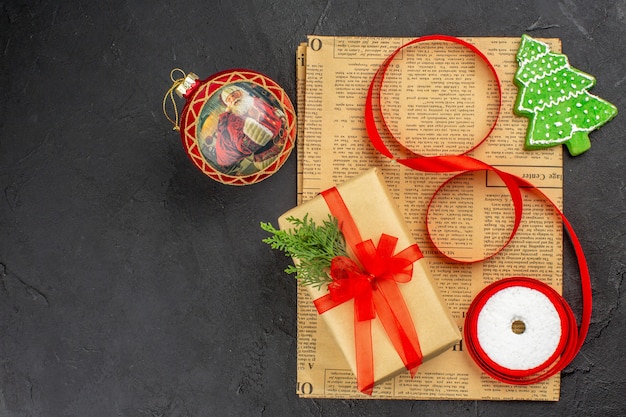 Top view xmas gift in brown paper branch fir ribbon on newspaper on dark surface