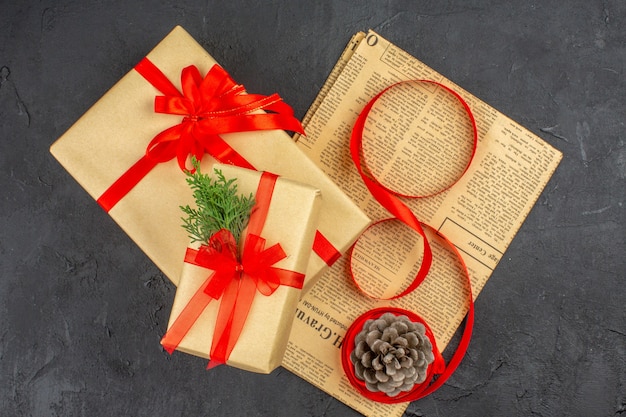 Вид сверху рождественский подарок в коричневой бумажной ветке еловой ленты на газетной шишке на темной поверхности