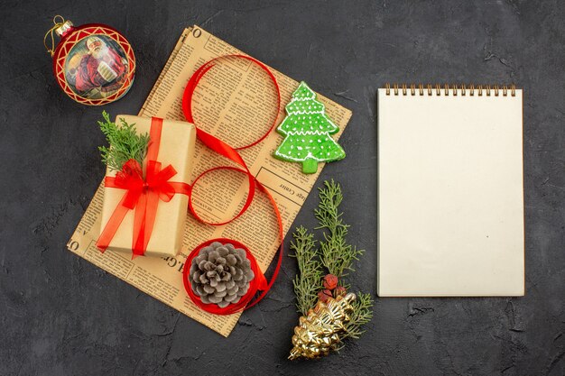 신문에 있는 갈색 종이 분기 전나무 리본의 상위 뷰 크리스마스 선물은 어두운 표면에 있는 노트북을 장식합니다.