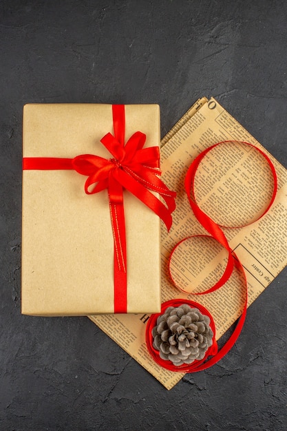 Free photo top view xmas gift in brown paper ribbon on newspaper on dark surface