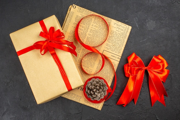 Top view xmas gift in brown paper ribbon on newspaper red bow on dark surface