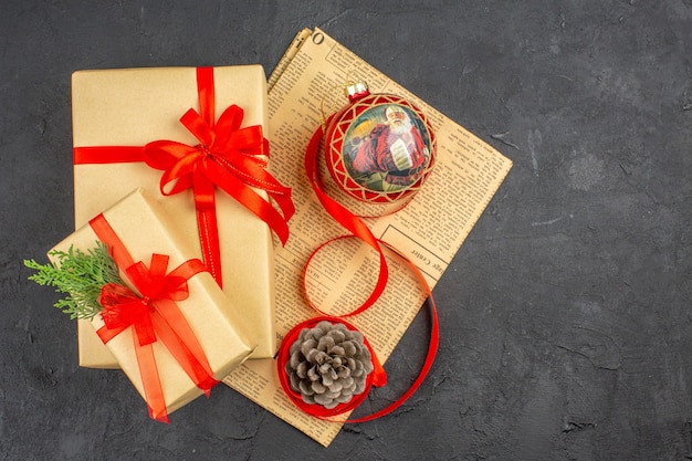 Free photo top view xmas gift in brown paper ribbon xmas tree toy on newspaper on dark surface