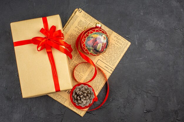 Вид сверху рождественский подарок в коричневой бумажной ленте елочная игрушка на газете на темной поверхности
