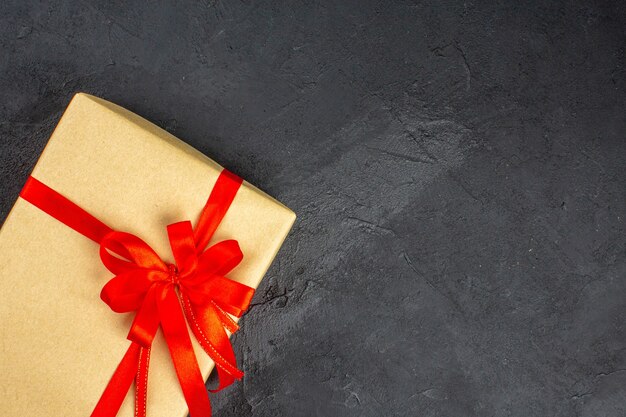 暗い表面に赤いリボンで結ばれた茶色の紙の上面のクリスマスプレゼント