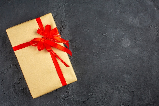 Рождественский подарок в коричневой бумаге, перевязанный красной лентой на темной поверхности, вид сверху