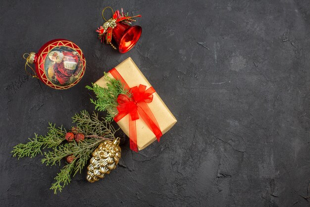 Рождественский подарок в коричневой бумаге, перевязанный красной лентой, елочные украшения на темном фоне, копировальное пространство