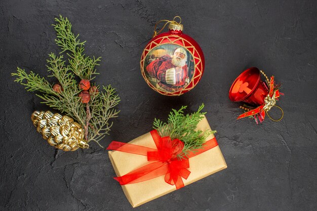 Top view xmas gift in brown paper tied with red ribbon xmas tree ornaments on dark surface