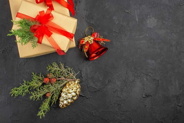 Вид сверху рождественский подарок в коричневой бумаге, перевязанный красной лентой, украшения рождественской елки на темной поверхности