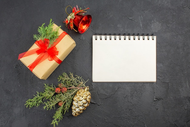 어두운 표면에 빨간 리본 크리스마스 트리 장식품 노트북으로 묶인 갈색 종이의 상위 뷰 크리스마스 선물