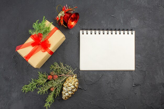 暗い表面に赤いリボンのクリスマスツリーの装飾品ノートブックで結ばれた茶色の紙の上面のクリスマスプレゼント