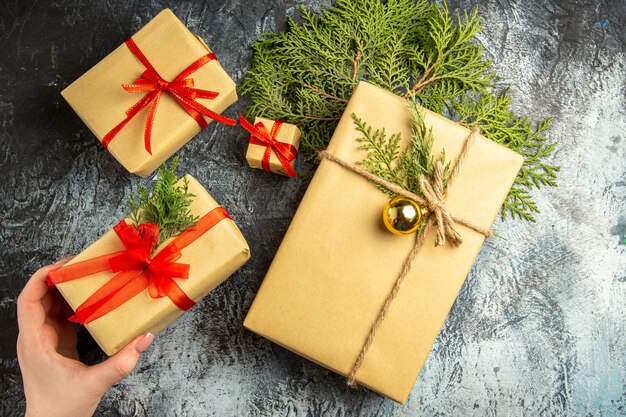 Top view xmas gift in woman hand small gifts pine branches on grey surface