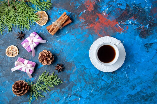 Top view xmas gifts fir tree branches cones anises cup of tea on blue background free place