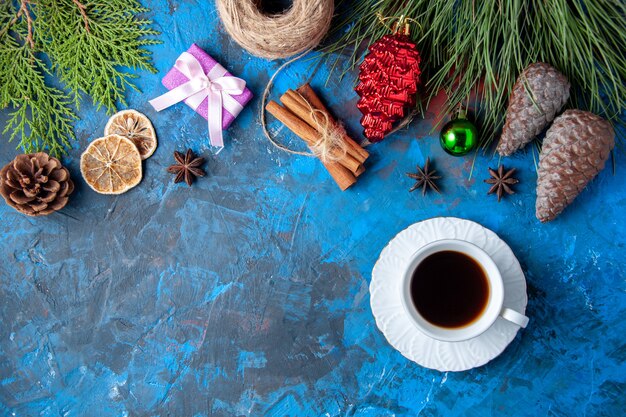 Top view xmas gifts fir tree branches cones anises a cup of tea on blue surface