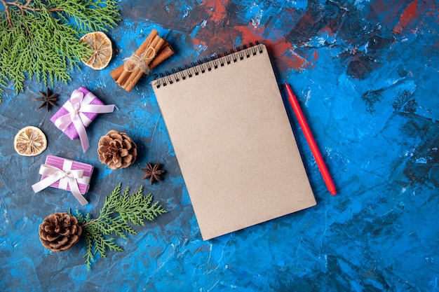 Top view xmas gifts fir tree branches cones anises notebook pencil on blue surface