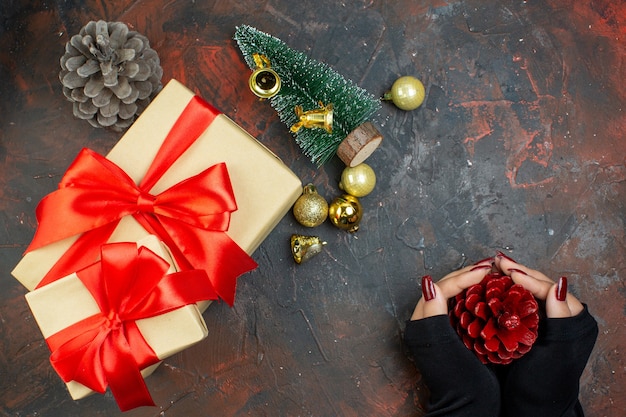 Free photo top view xmas gifts golden xmas balls red pinecone in woman hands small xmas tree on dark red table