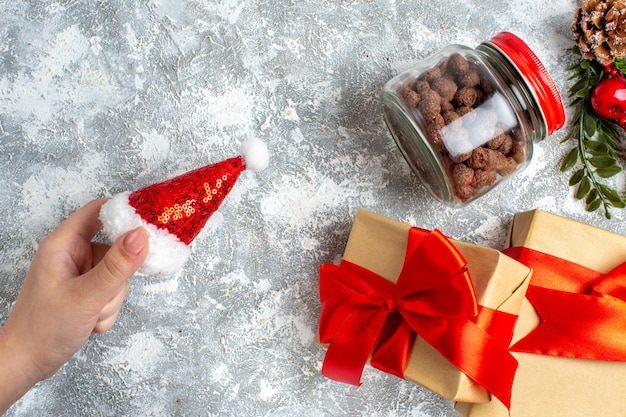 Vista dall'alto regali di natale cappello di babbo natale in cereali a mano femminile in barattolo sul tavolo grigio