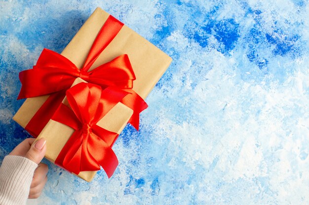 Top view xmas gifts tied with red bow in female hand on blue table with free space