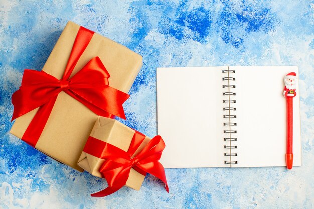 青いテーブルのメモ帳に赤い弓ペンで結ばれた上面図のクリスマスプレゼント