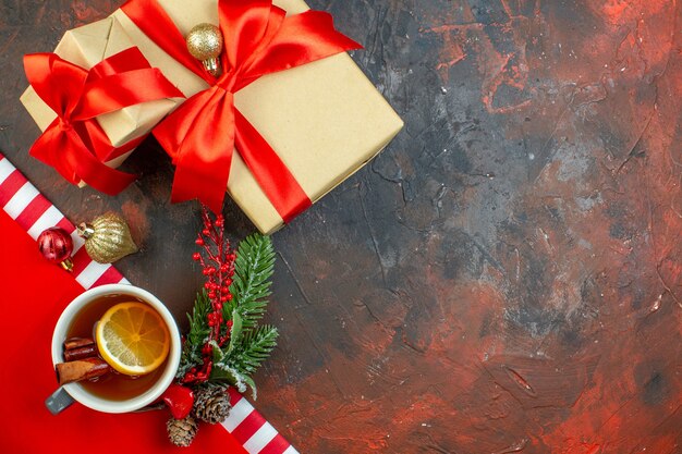Вид сверху рождественские подарки, перевязанные красной лентой, ветка рождественского дерева, чашка чая на темно-красном столе, место для копирования