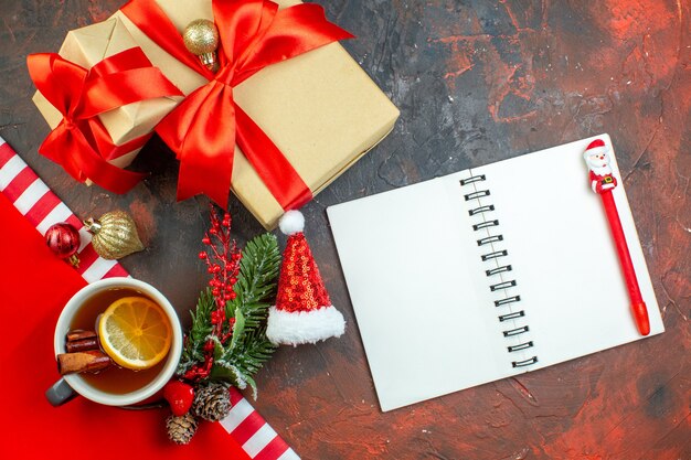 Top view xmas gifts tied with red ribbon xmas tree branch notebook red pen on dark red table