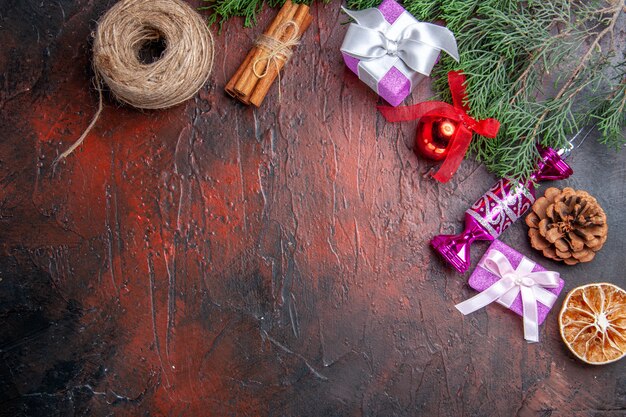 Top view xmas gifts tree branch with cone xmas tree toys cinnamon straw thread on dark red background