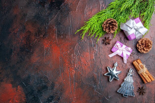 Top view xmas gifts with pink box and white ribbon tree branch anises cinnamon xmas tree toys on dark red background
