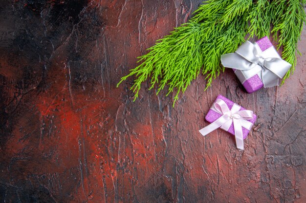 Top view xmas gifts with pink box and white ribbon tree branch on dark red background