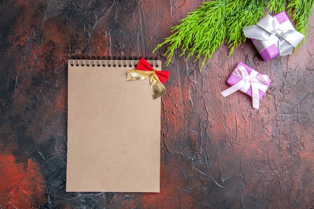 Top view xmas gifts with pink box and white ribbon tree branch a notebook on dark red surface