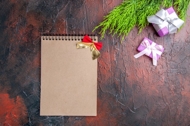 Top view xmas gifts with pink box and white ribbon tree branch a notebook on dark red surface