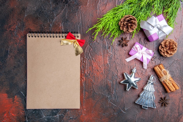 Top view xmas gifts with pink boxes and white ribbon tree branches anises cinnamon xmas tree toys a notebook on dark red surface