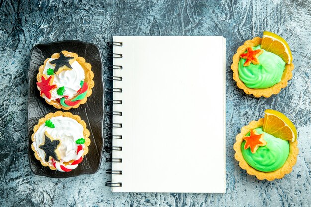 Top view xmas tarts on black plate xmas candy notebook on grey table