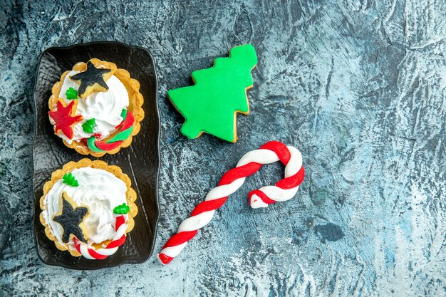 Вид сверху рождественские пироги на черной тарелке рождественские конфеты и рождественское печенье на сером столе
