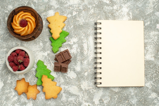 Top view xmas tree cookies bowl with raspberries notebook chocolates on grey table