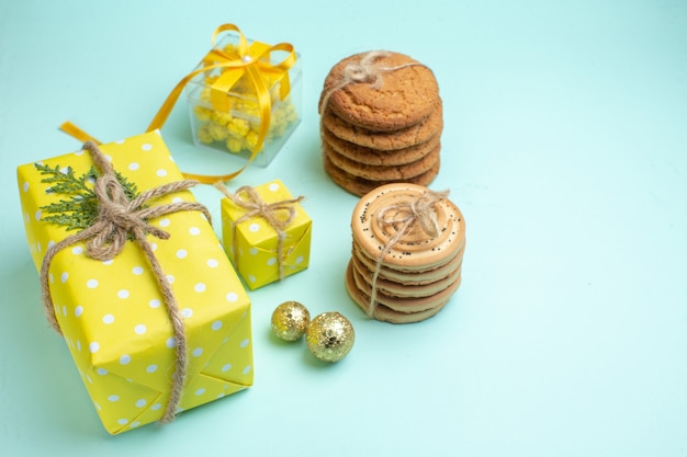 Top view of xsmas mood with stacked various delicious cookies and beautiful yellow gift boxes next to decoration accessory on pastel green background
